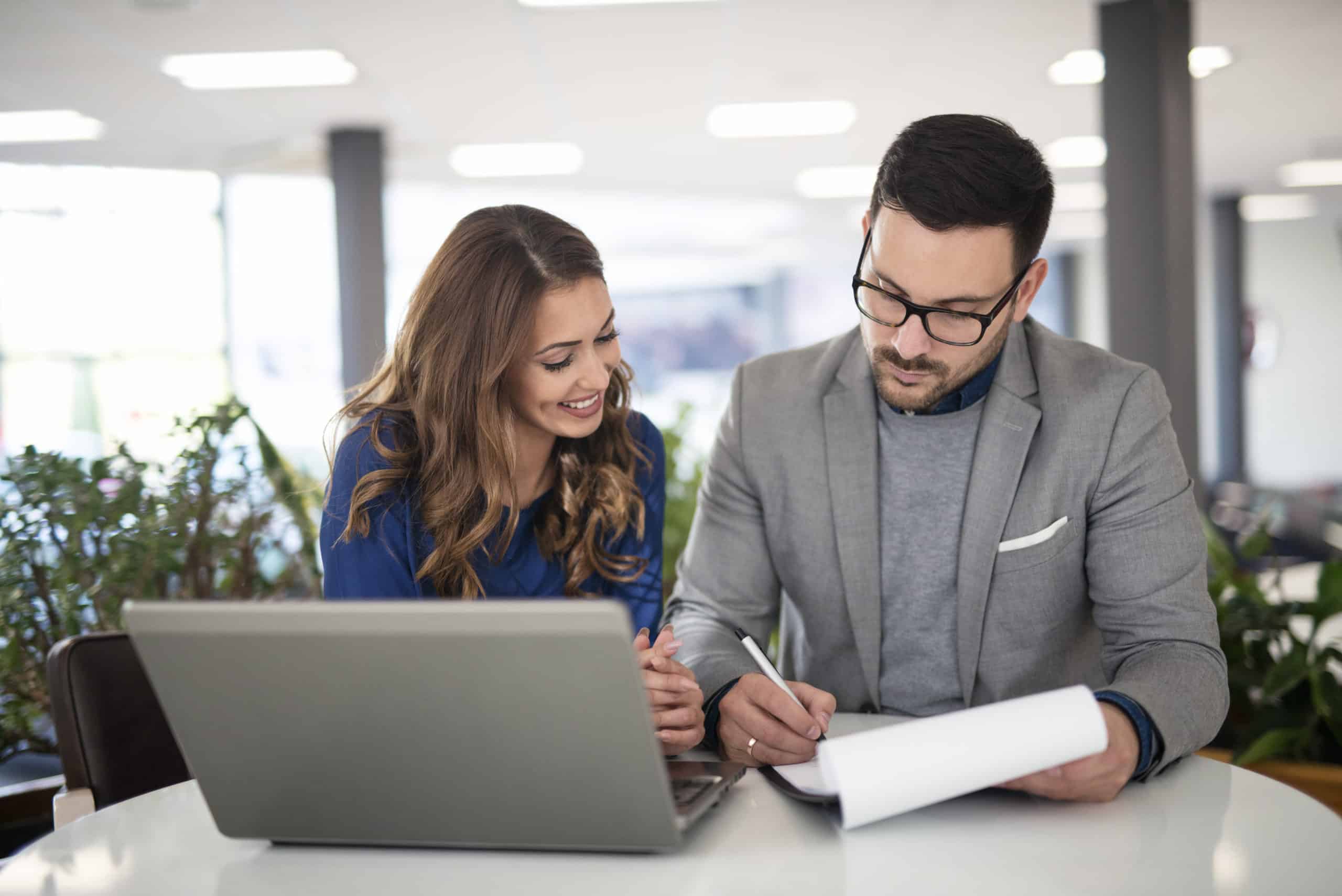 Two colleagues reviewing a document next to an open laptop