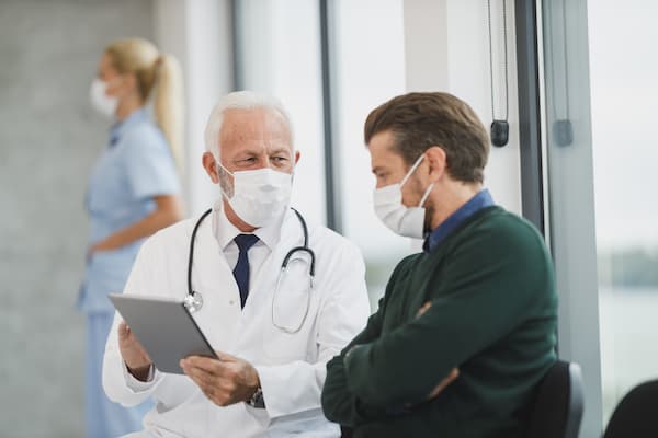 Masked doctor and patient reviewing information on a tablet