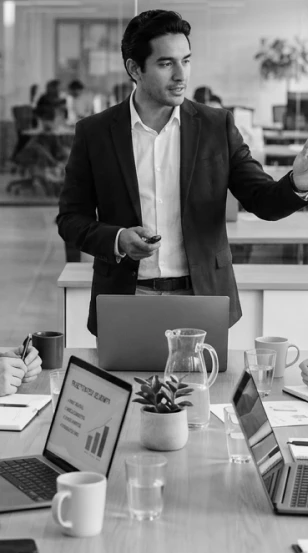 Presenter standing at a conference table with colleagues working on laptops