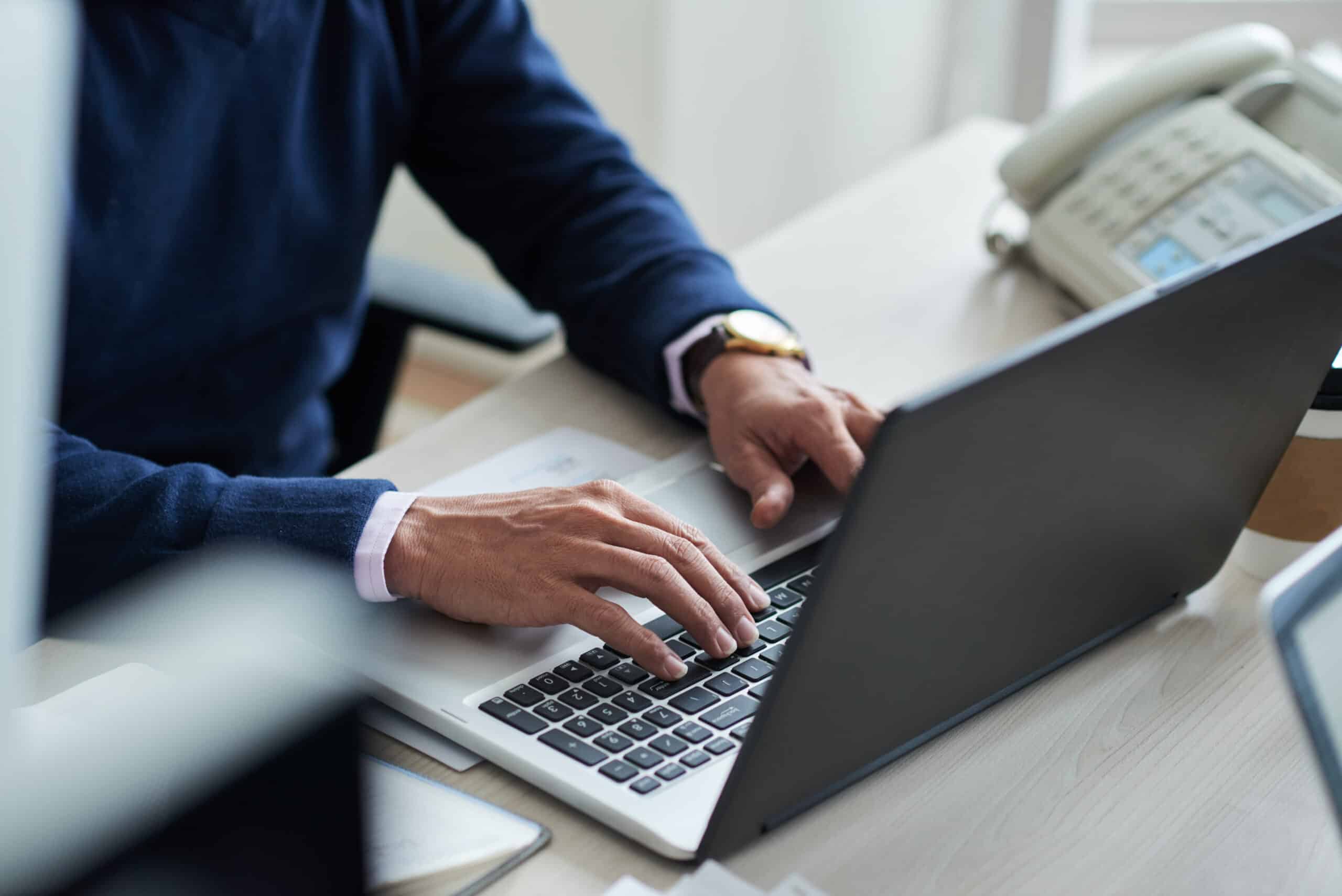 Hands typing on a laptop beside a desk phone