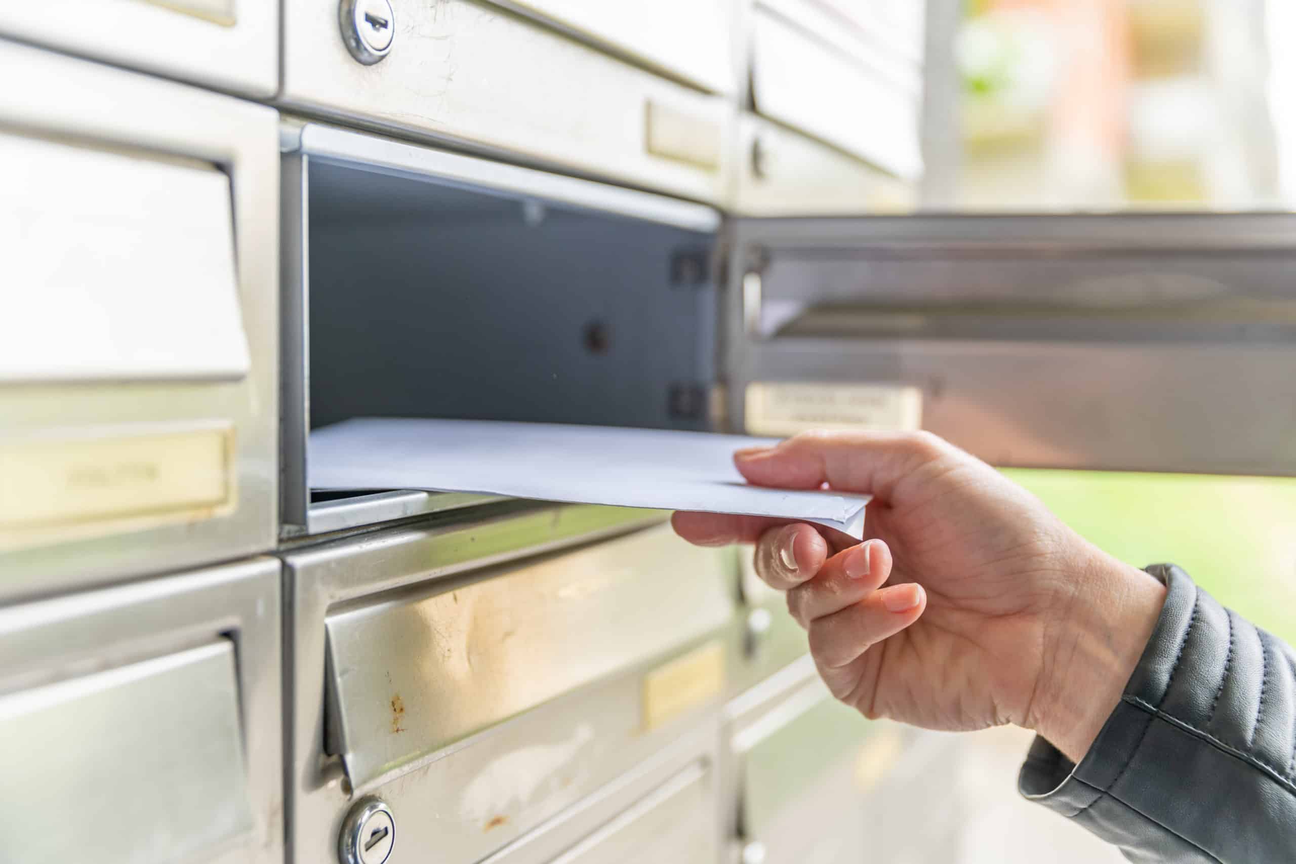 Hand placing an envelope into an apartment mailbox