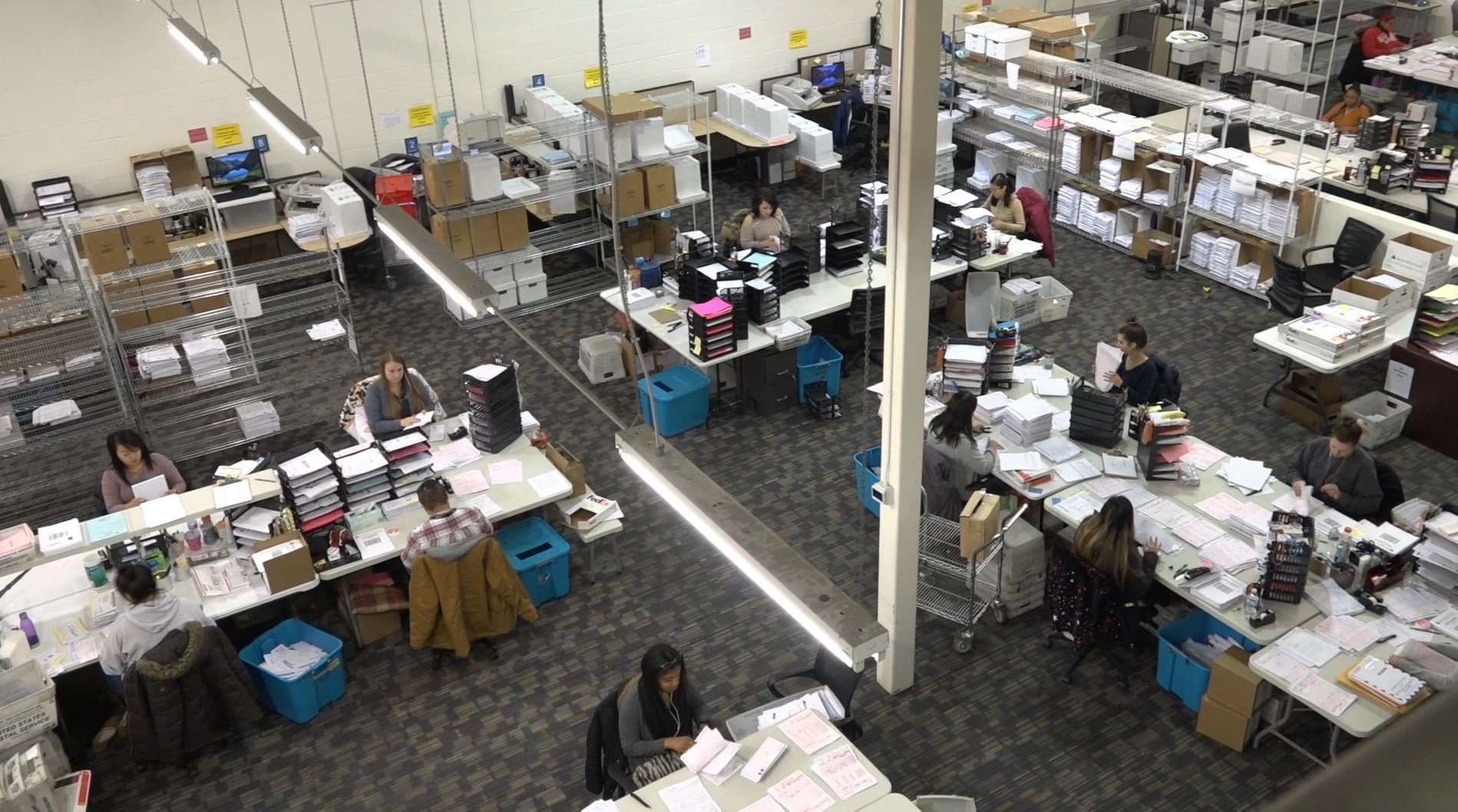 Overhead view of staff sorting paper mail and documents in a large mailroom