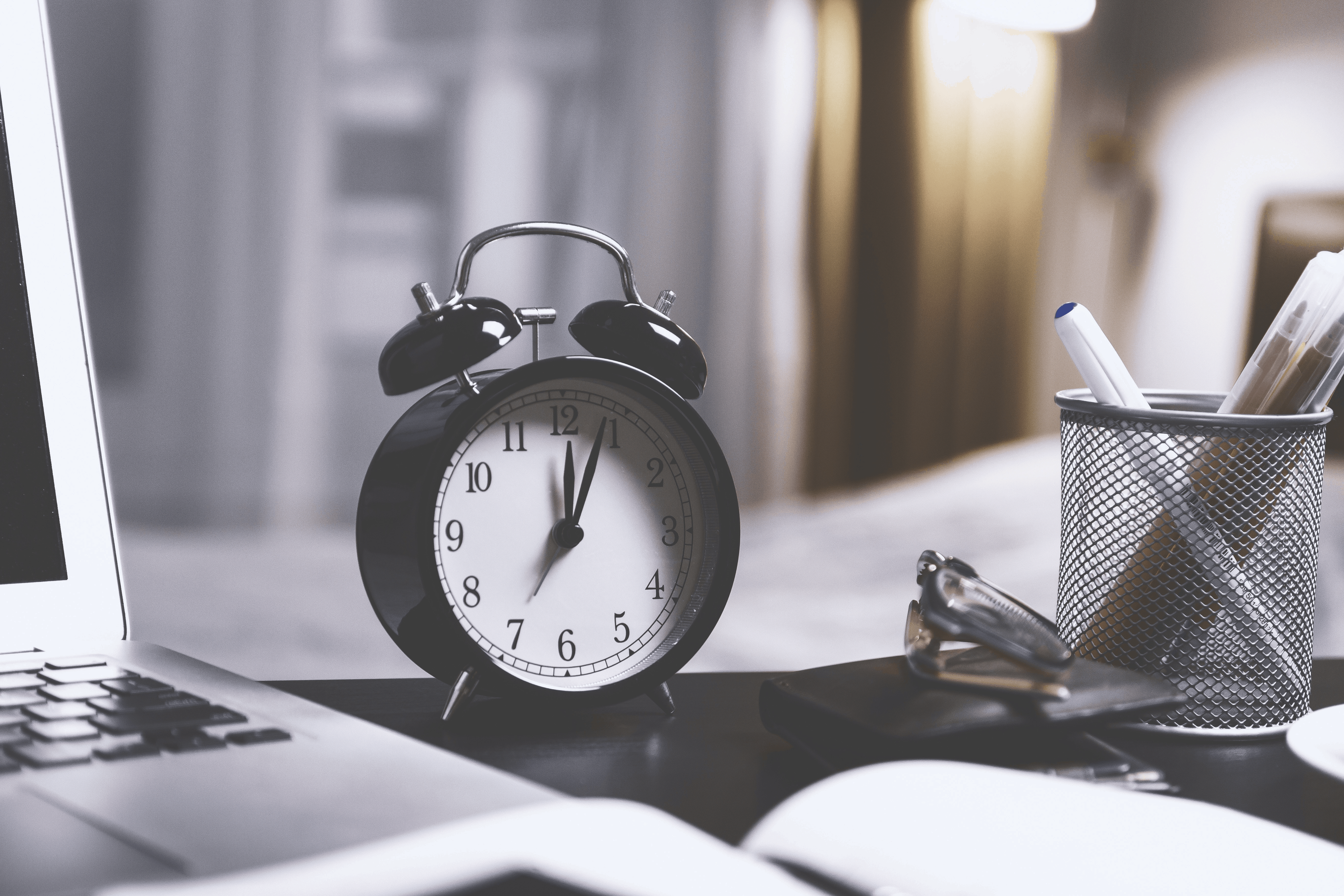 Alarm clock on a desk next to a laptop and pen cup