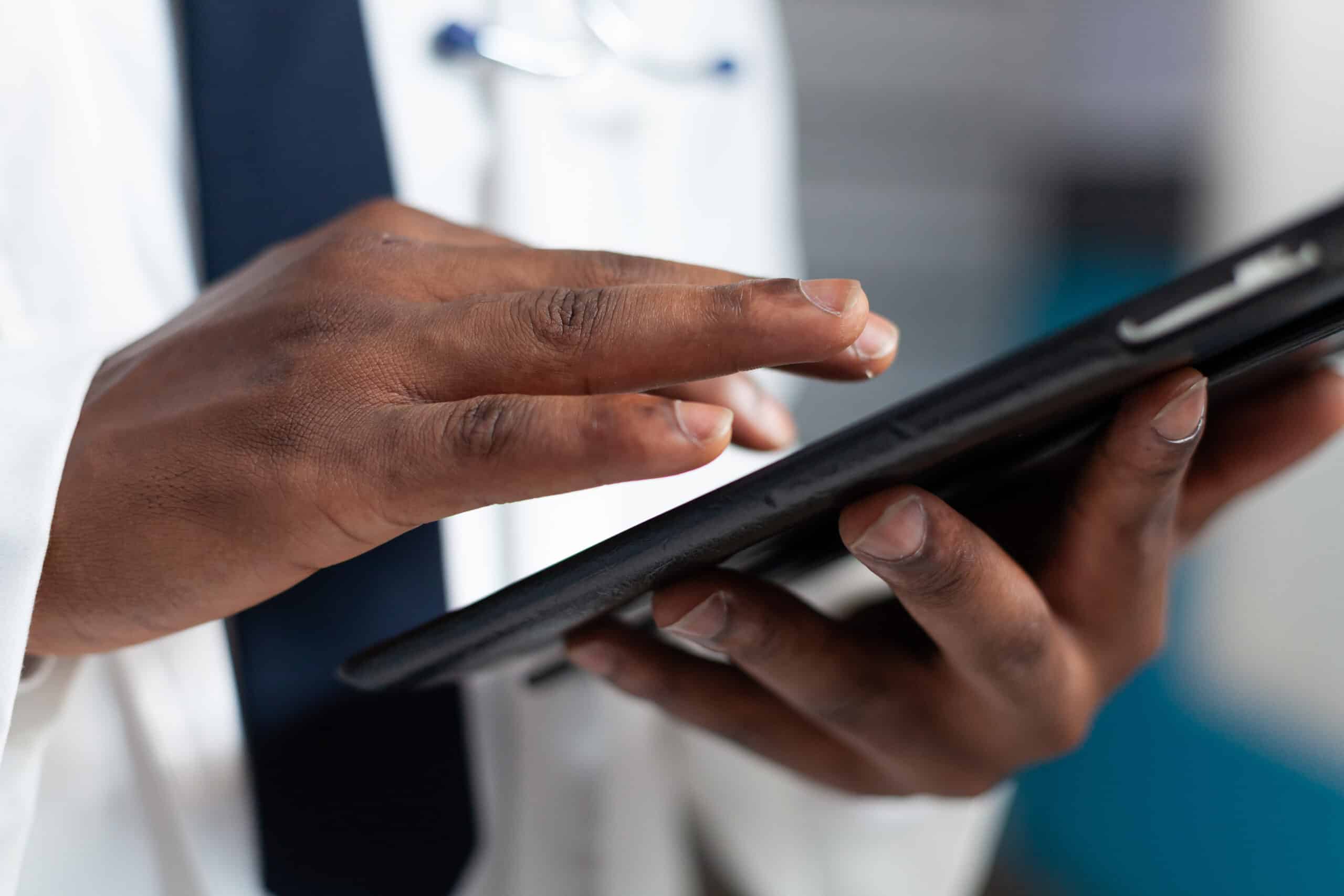 Closeup of african american doctor holding tablet computer typing healthcare treatment